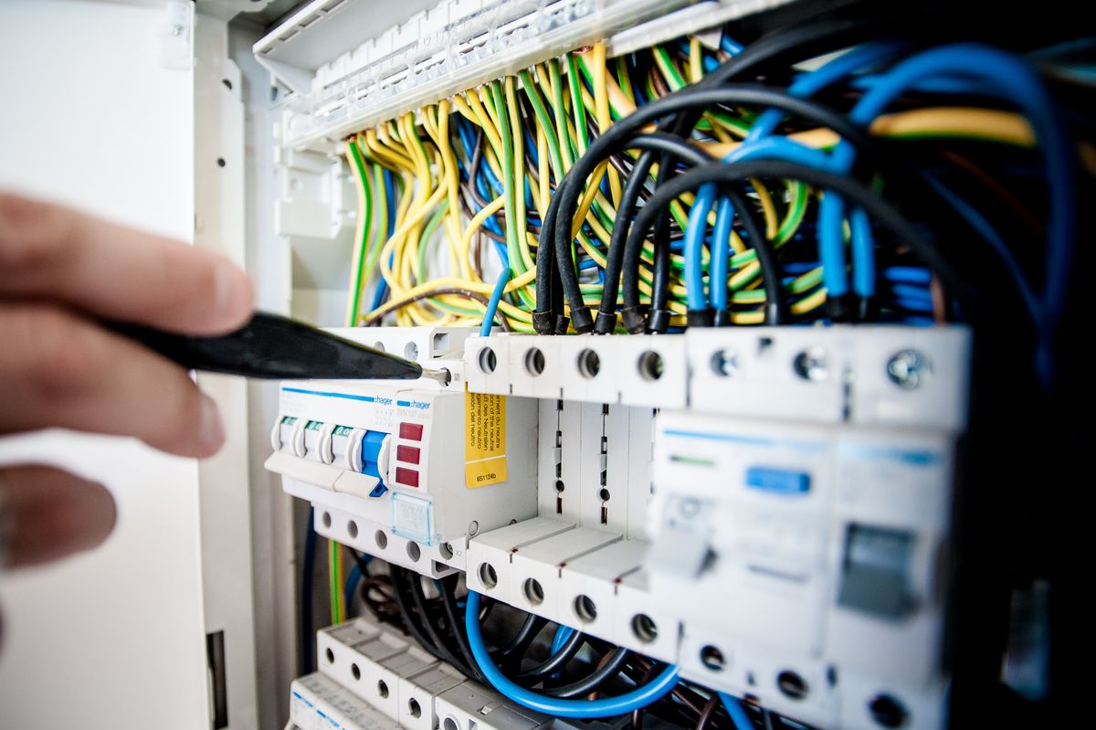 Un électricien intervient dans un tableau électrique ouvert, fils colorés visibles
