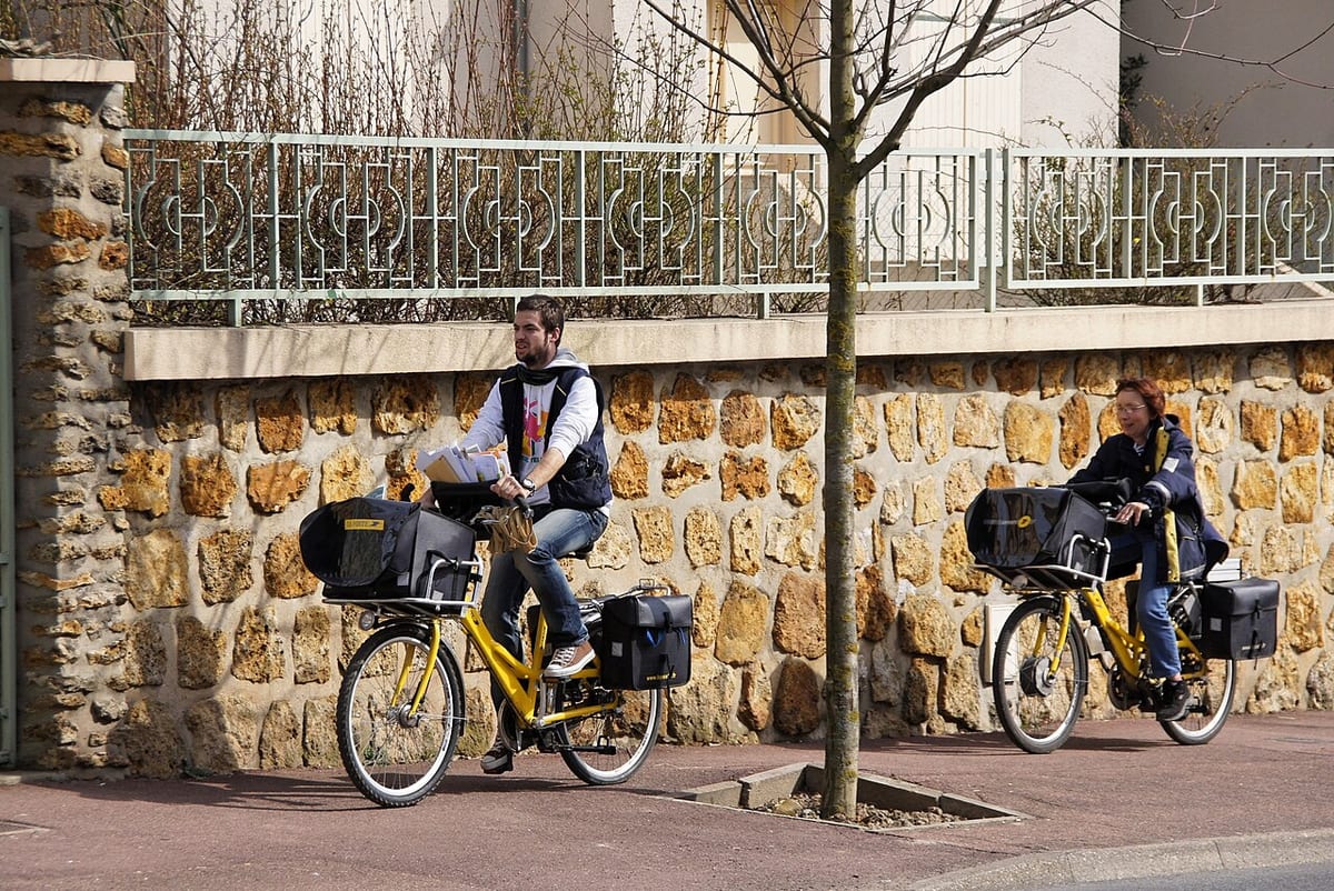 Un facteur en tournée à vélo, sacoches chargées de courrier