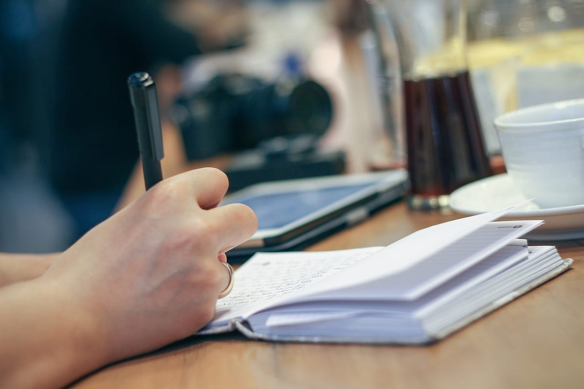 Un carnet de notes ouvert sur un bureau, stylo en main