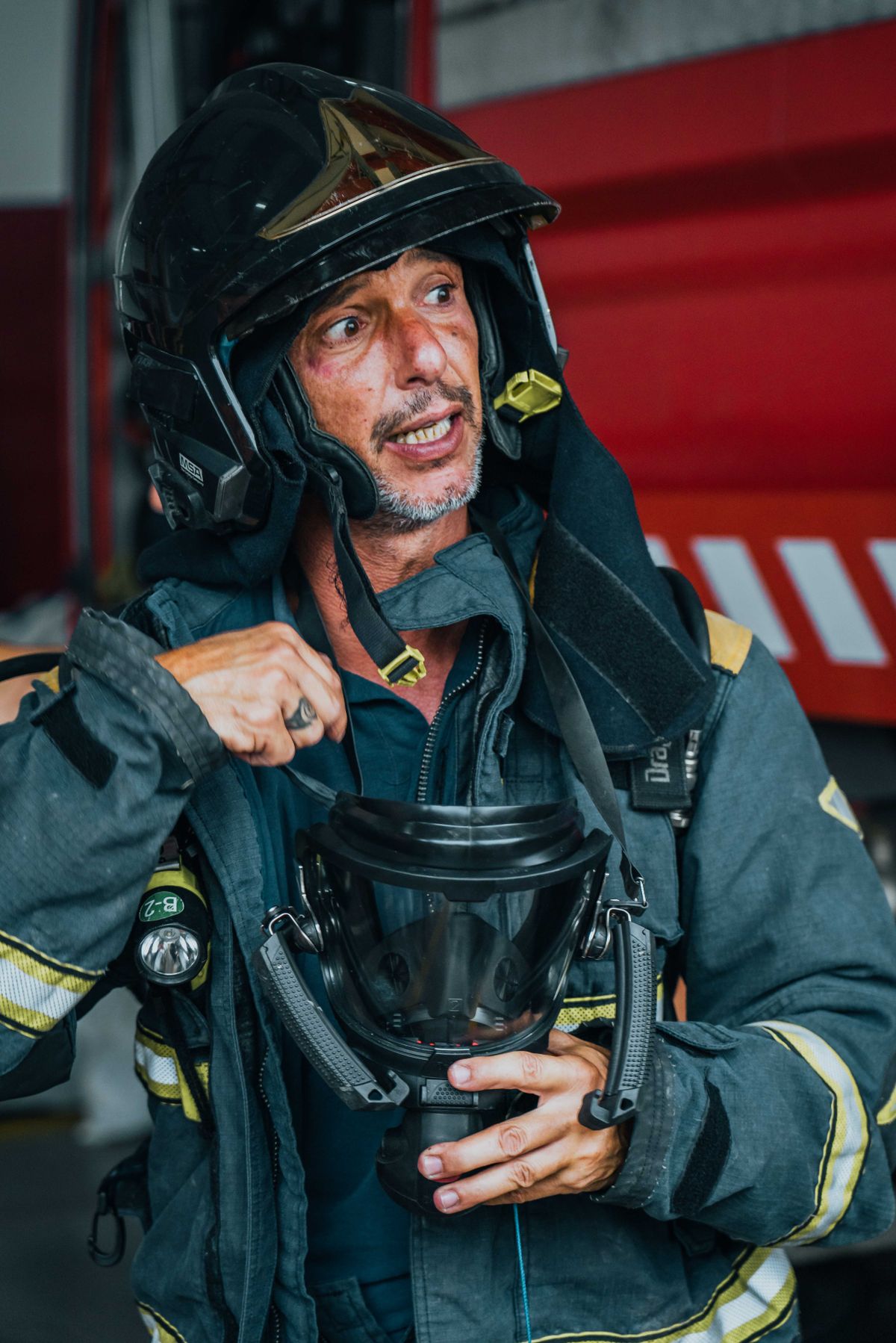 Un sapeur-pompier en tenue d'intervention, casque à la main, près des véhicules de la caserne