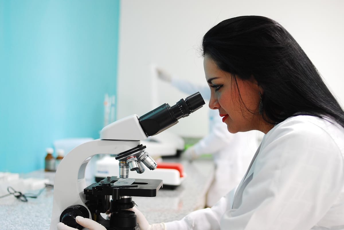 Une technicienne biologiste observe un échantillon au microscope